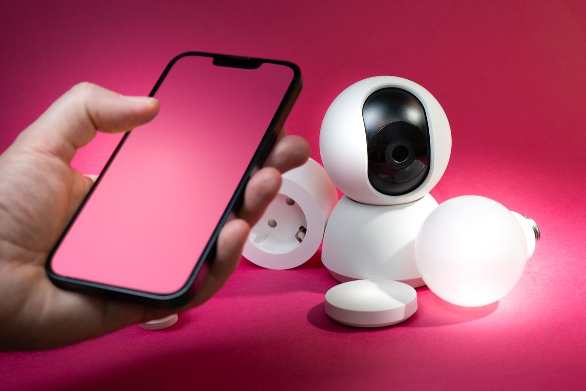 A smartphone beside connected home security and lighting devices