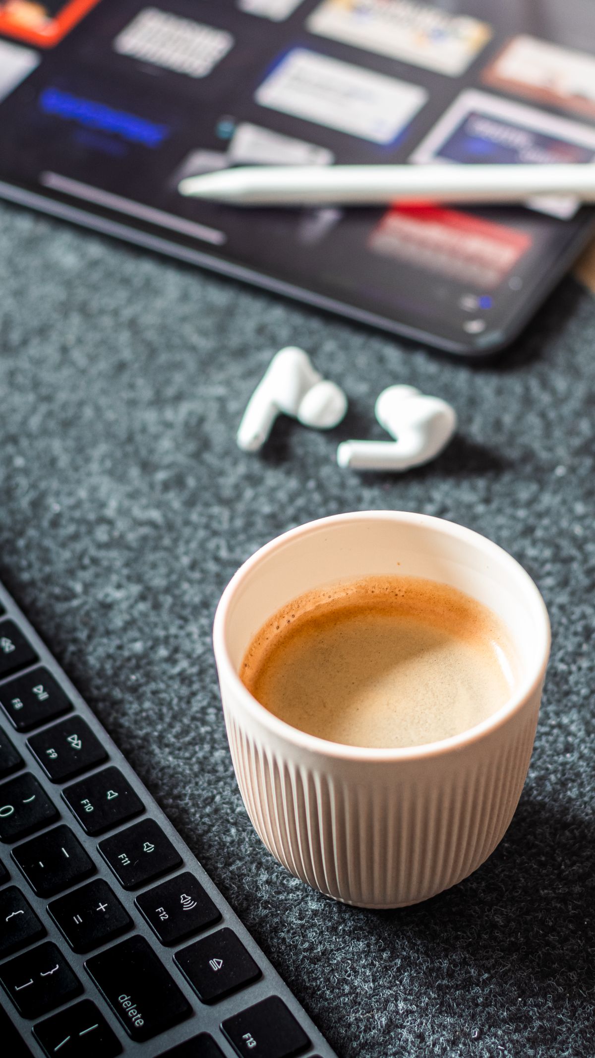 Coffee and earbuds beside a laptop keyboard on a work desk