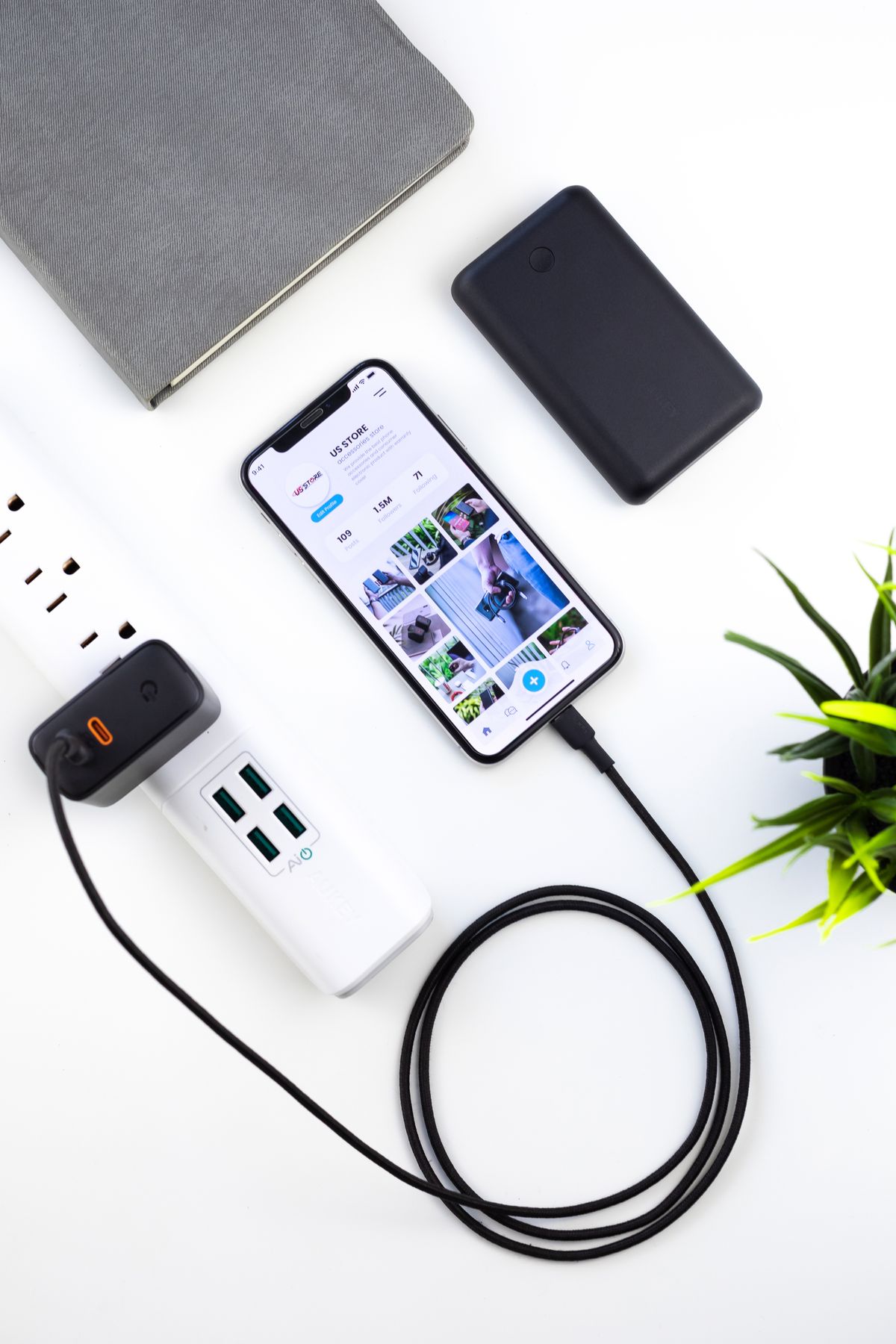 A smartphone charging on a white desk beside a tablet and plant
