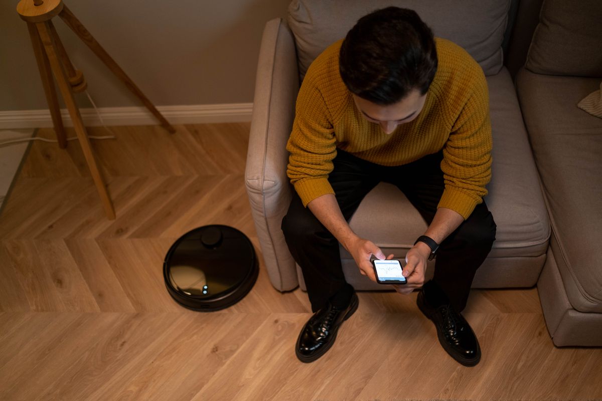 A person using a phone beside a robot vacuum in a living room