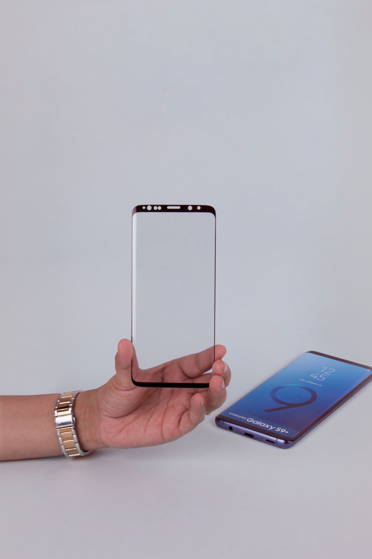 A hand holding a tempered glass screen protector beside a smartphone