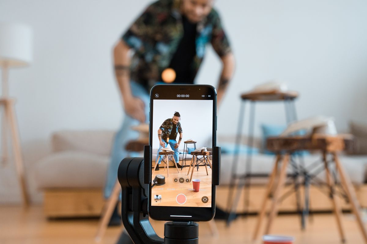 A person recording a video with a smartphone on a tripod in a living room