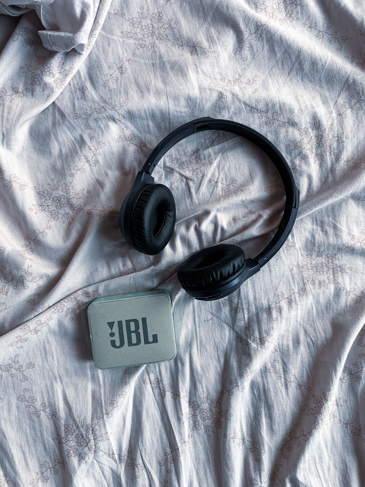 A portable speaker and wireless headphones resting on textured fabric