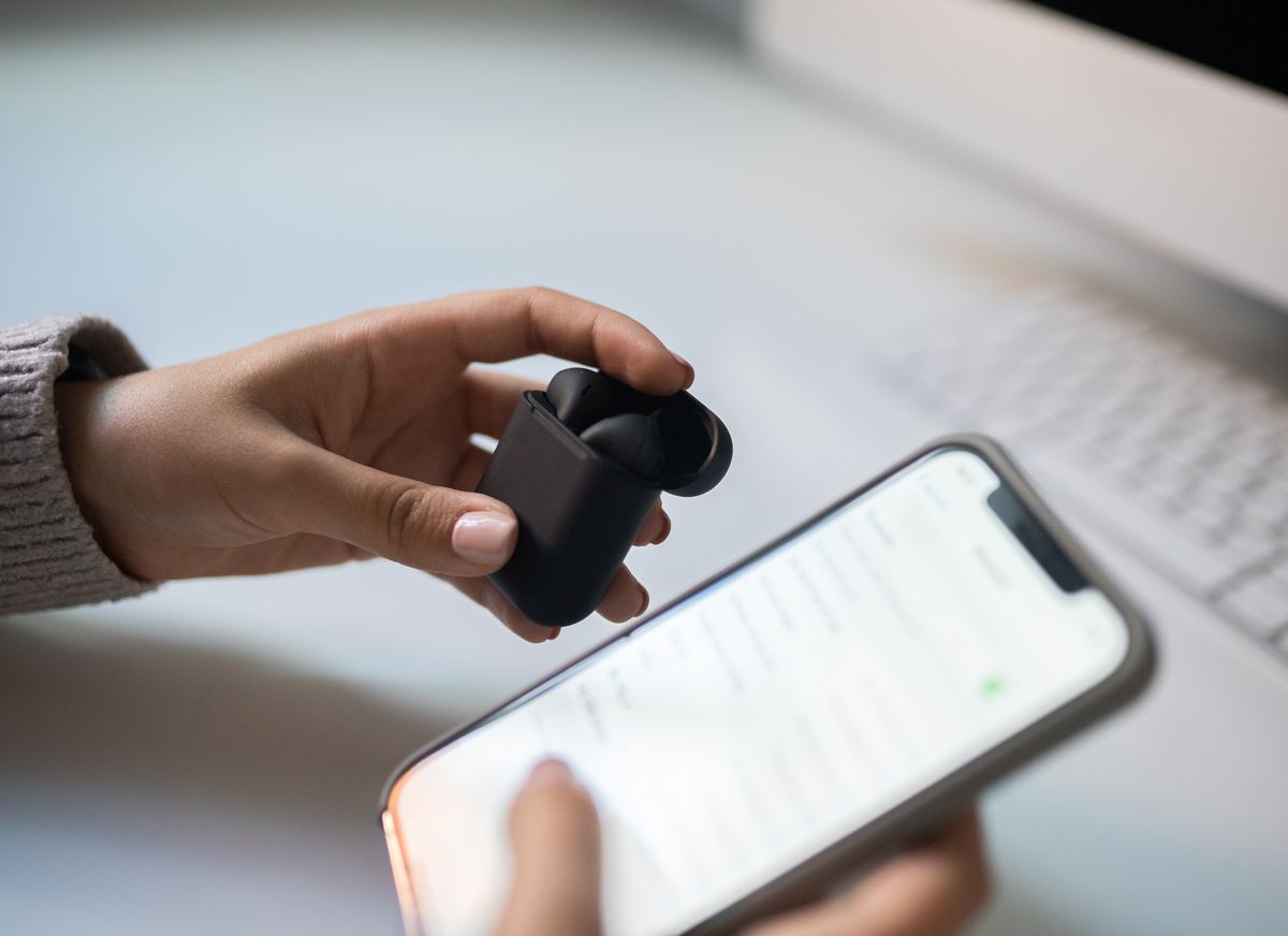 Hands holding wireless earbuds beside a smartphone