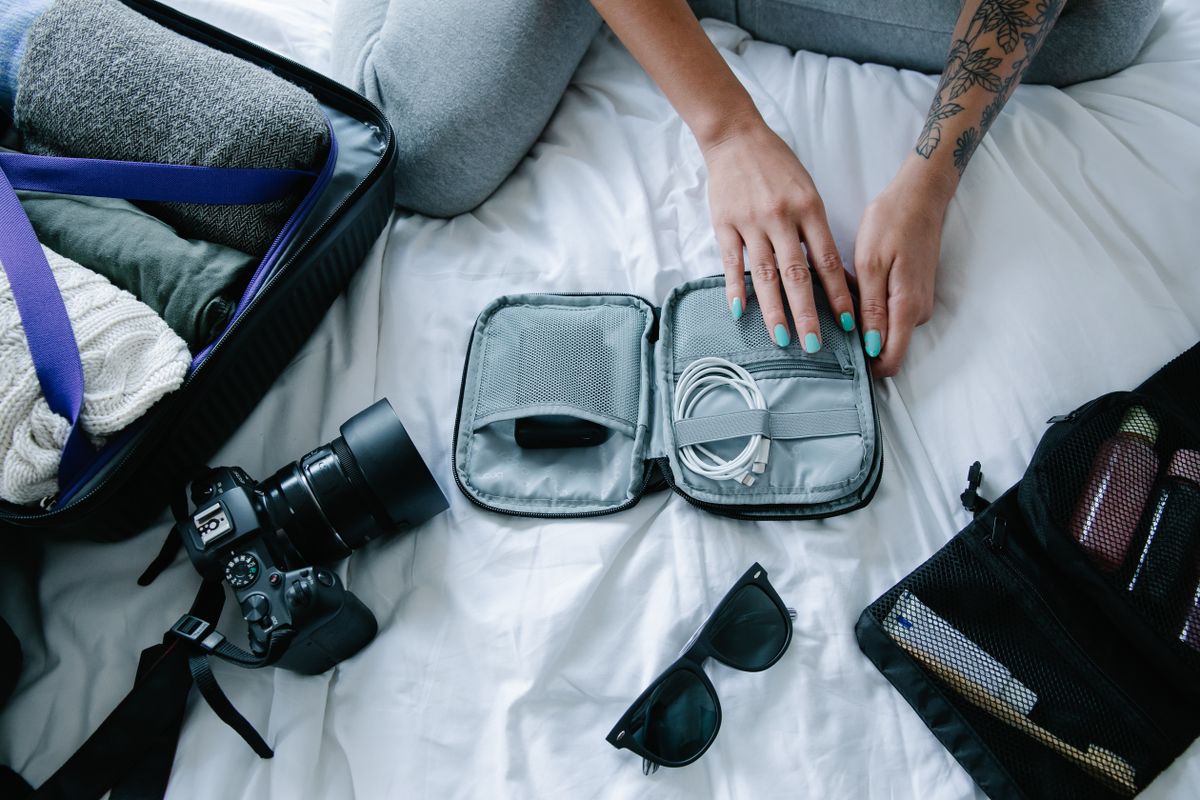 Hands packing cables, a camera and accessories into travel luggage